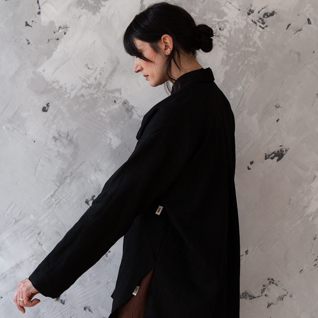 Person wearing a black coat against a textured gray wall
