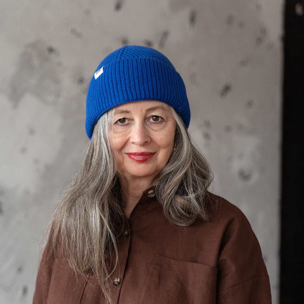 Person wearing a blue beanie and brown jacket against a textured wall.