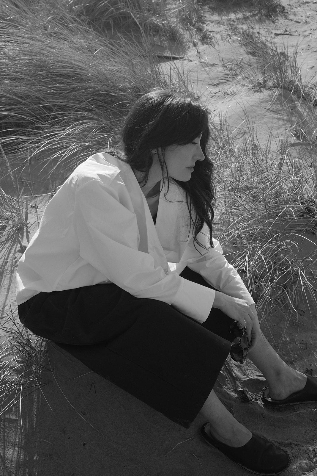 Person sitting on a rock in a natural setting with grass and sand.