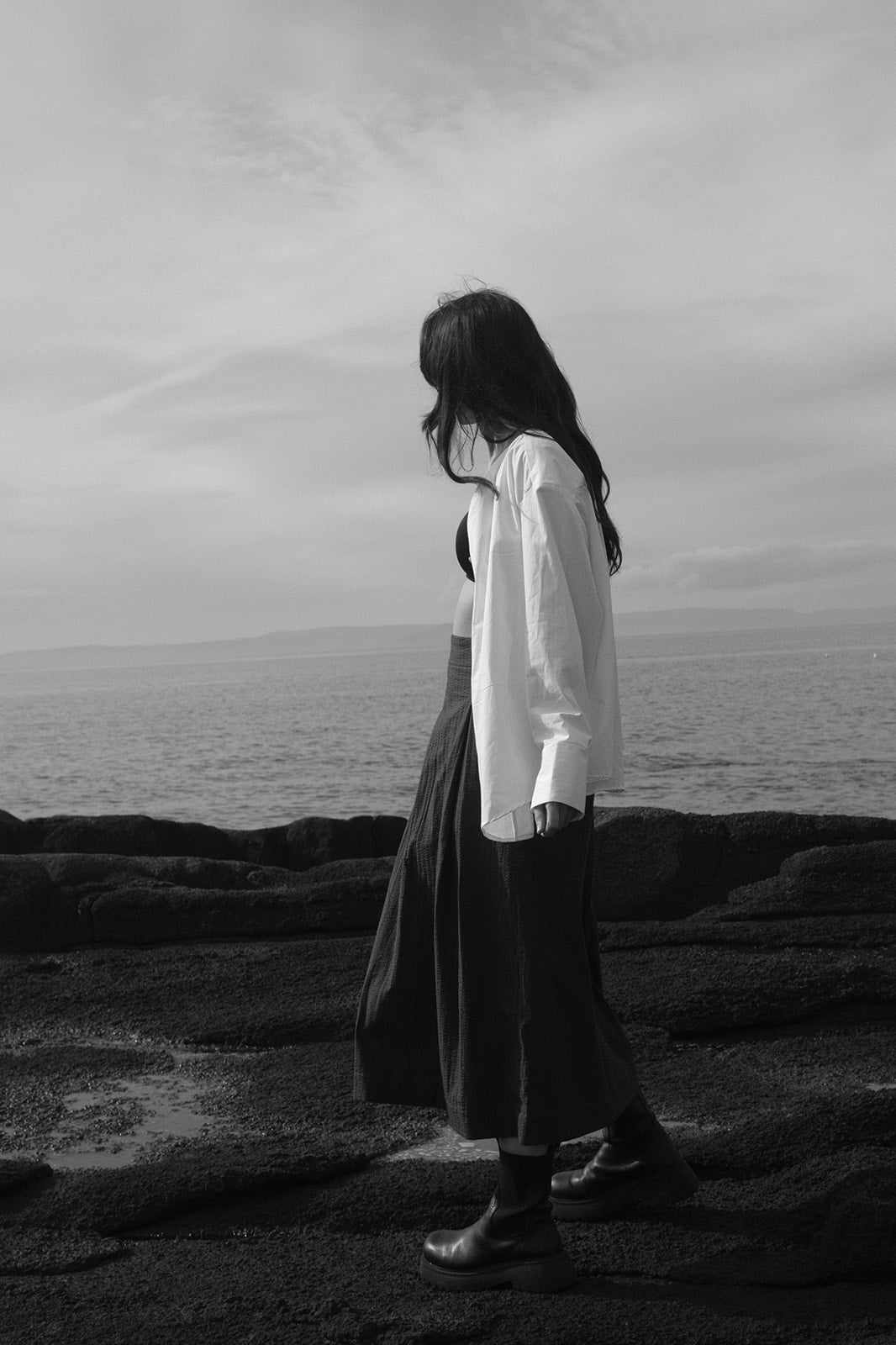 Person standing on a rocky shore with ocean and sky in the background