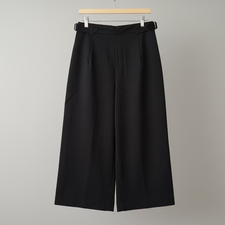 Black wide-leg pants hanging on a wooden hanger against a white wall.