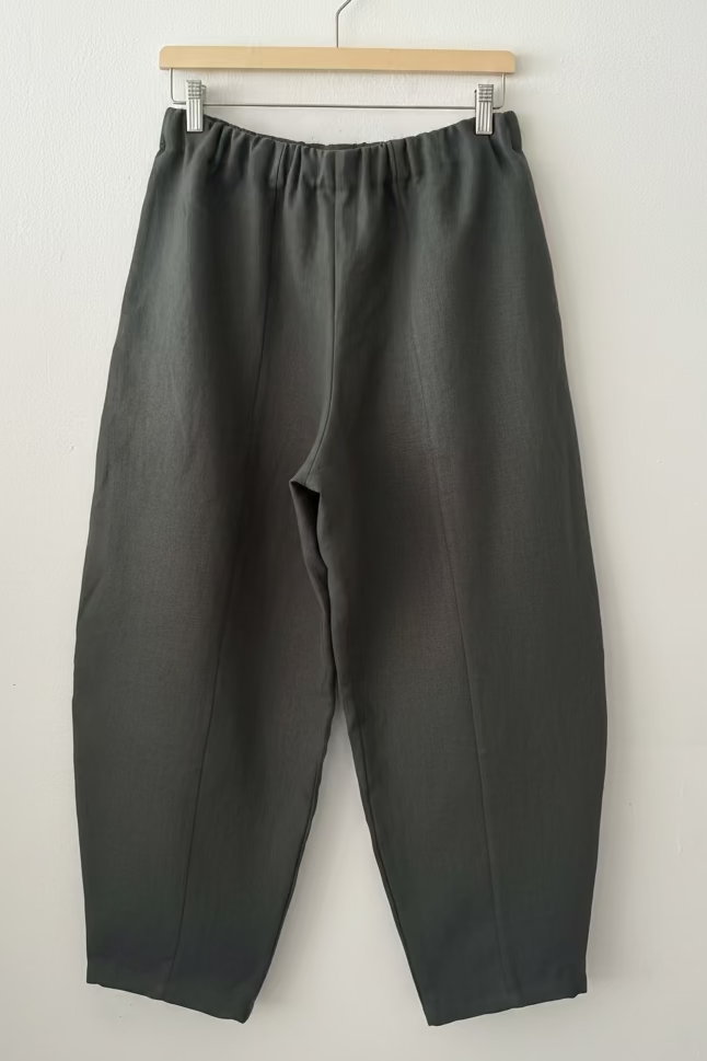 Dark gray pants on a wooden hanger against a white wall