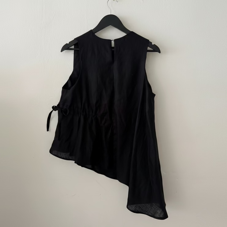 Black sleeveless top on a hanger against a white wall
