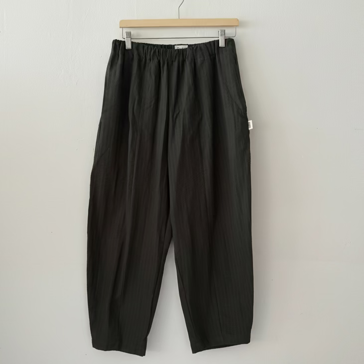 Black pants hanging on a wooden hanger against a white wall