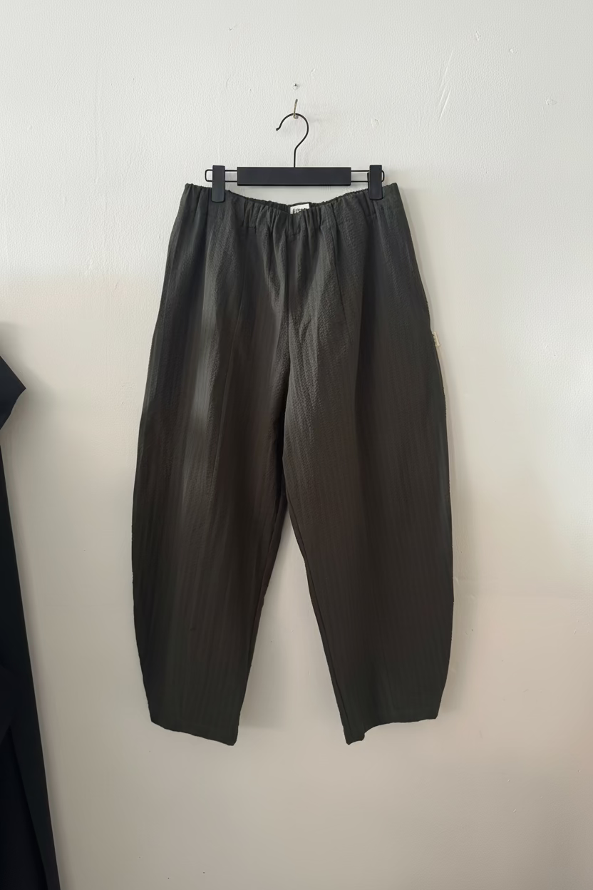 Dark gray pants hanging on a hanger against a white wall