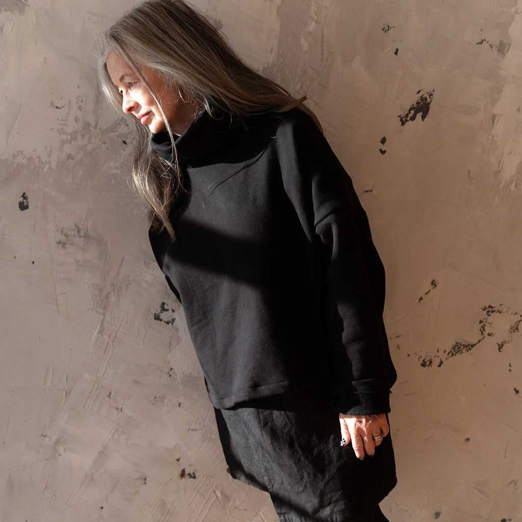 Woman wearing a black outfit against a textured wall.