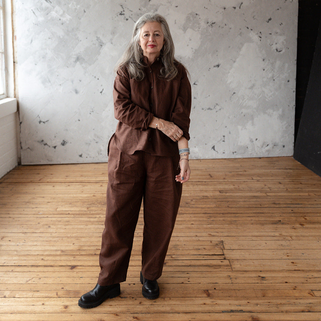 Person wearing a brown outfit standing in a room with wooden flooring and a textured white wall.