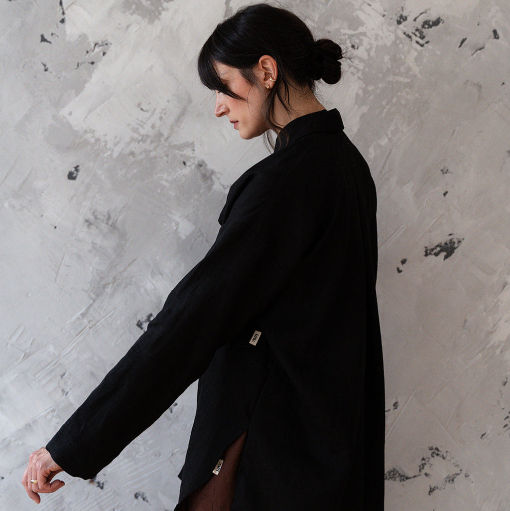 Person wearing a black coat against a textured gray wall