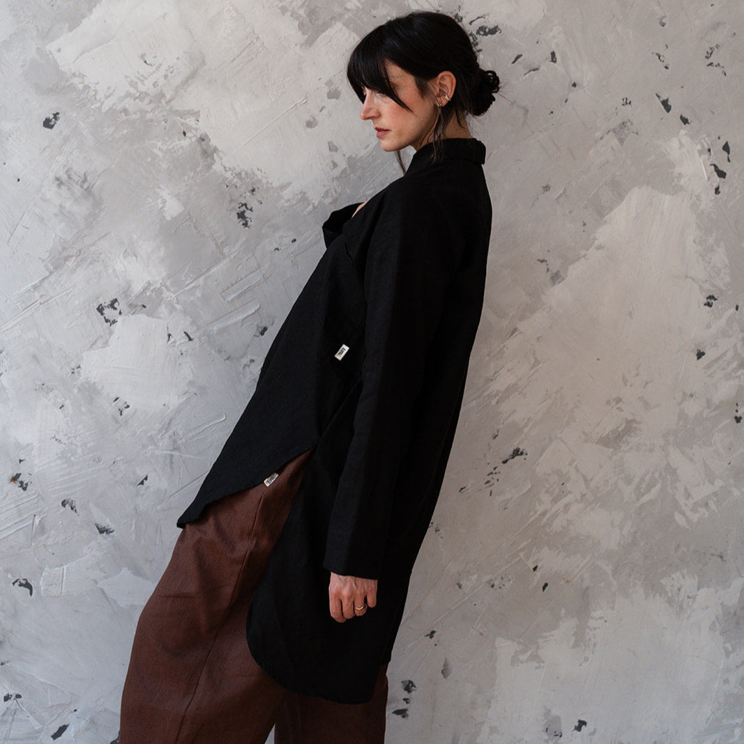 Person wearing a black coat and brown pants against a textured white wall