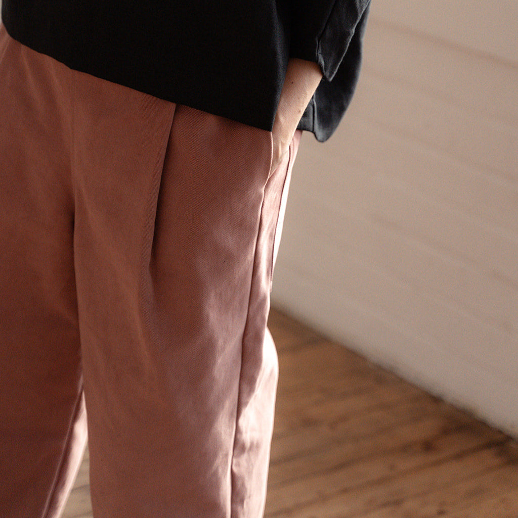 Person wearing a black top and brown pants standing in a room with wooden flooring.