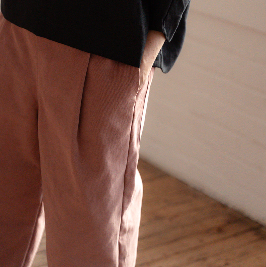 Person wearing a black top and brown pants standing in a room with wooden flooring.