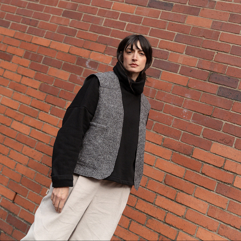 Person wearing a black sweater and gray vest against a brick wall