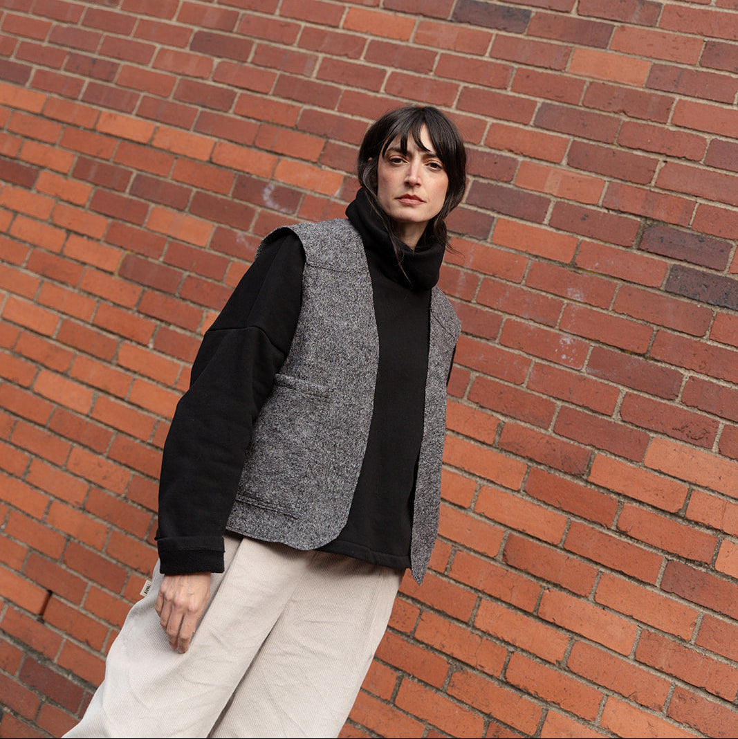 Person wearing a black sweater and gray vest against a brick wall
