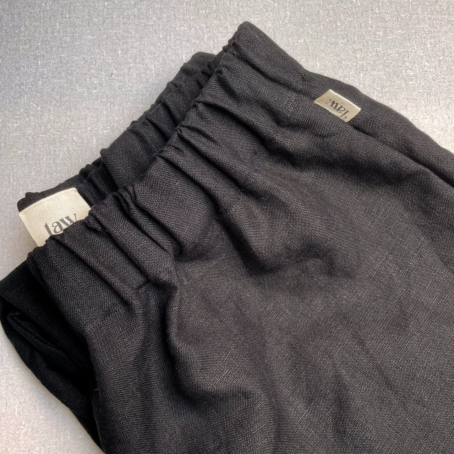 CLOSE UP OF BLACK LINEN TROUSERS WITH COTTON TAB