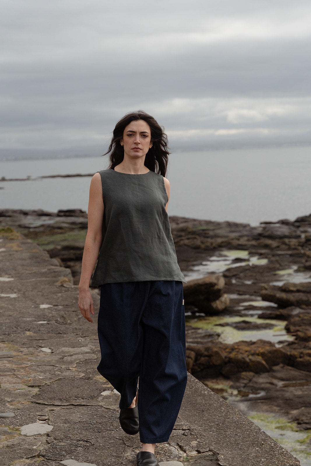 Woman walking along a rocky path by the ocean under a cloudy sky