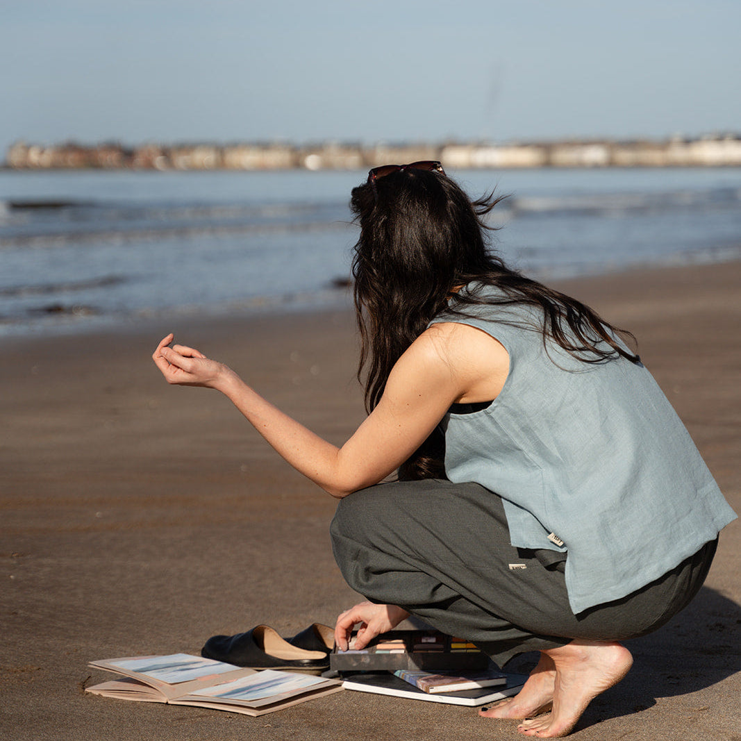 girl crouching on the beach with light blue linen vest on