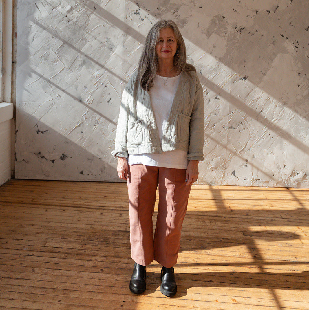 LAW Design studio Woman standing in a sunlit room with wooden floor and textured wall.