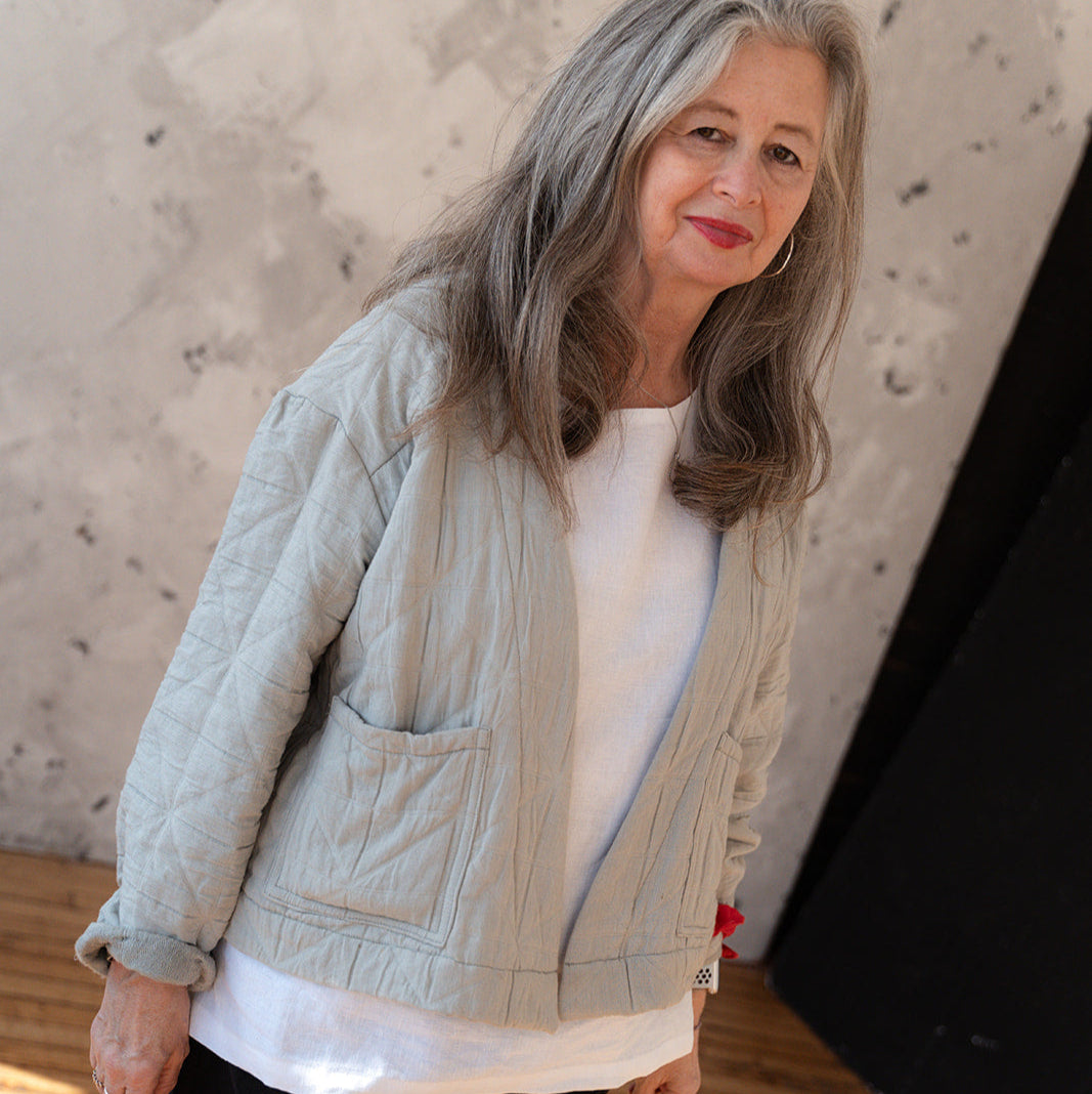 LAW Design studio Woman wearing a light green quilted jacket and black pants standing against a textured wall.