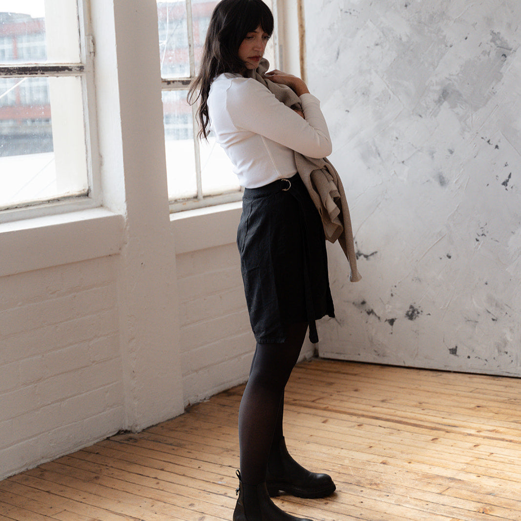 Woman standing in a room with large windows and a textured wall.