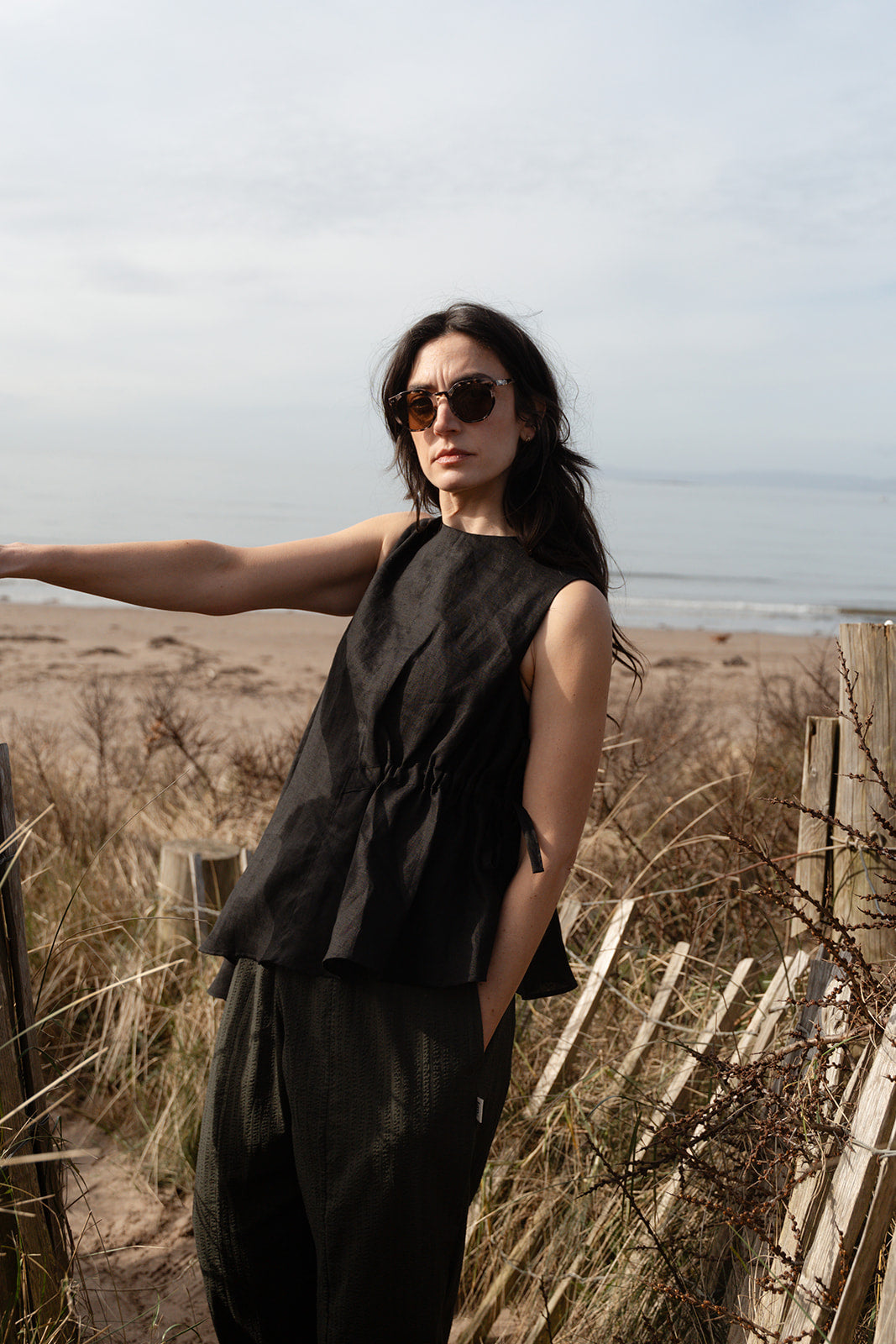 Woman in a black outfit standing on a beach with ocean in the background