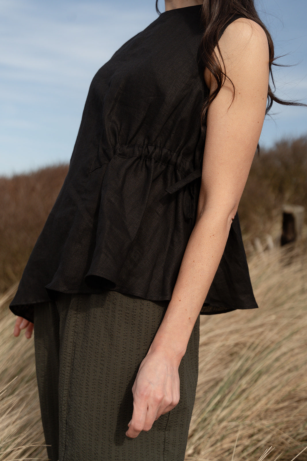 Person wearing a black sleeveless top and green skirt standing in a field with a blurred background