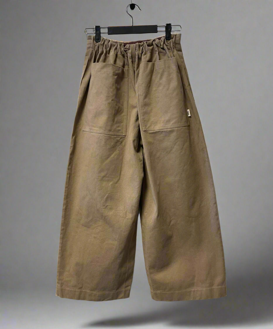 Brown wide-leg pants hanging on a hanger against a gray background