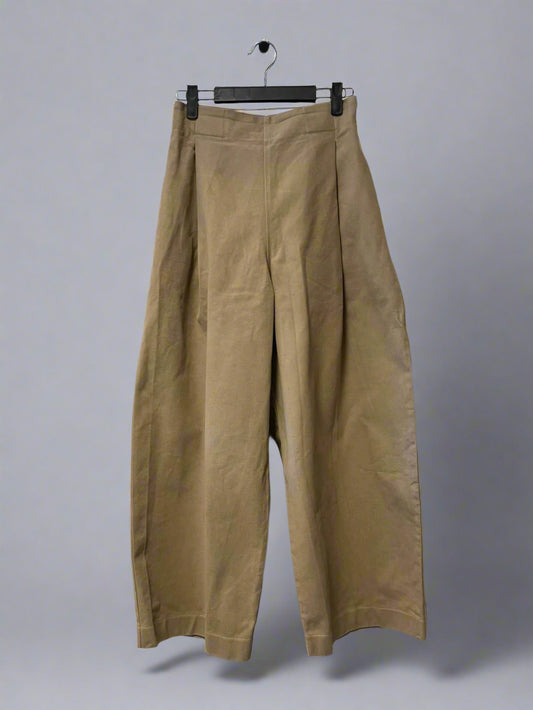 Beige pants hanging on a hanger against a white wall.