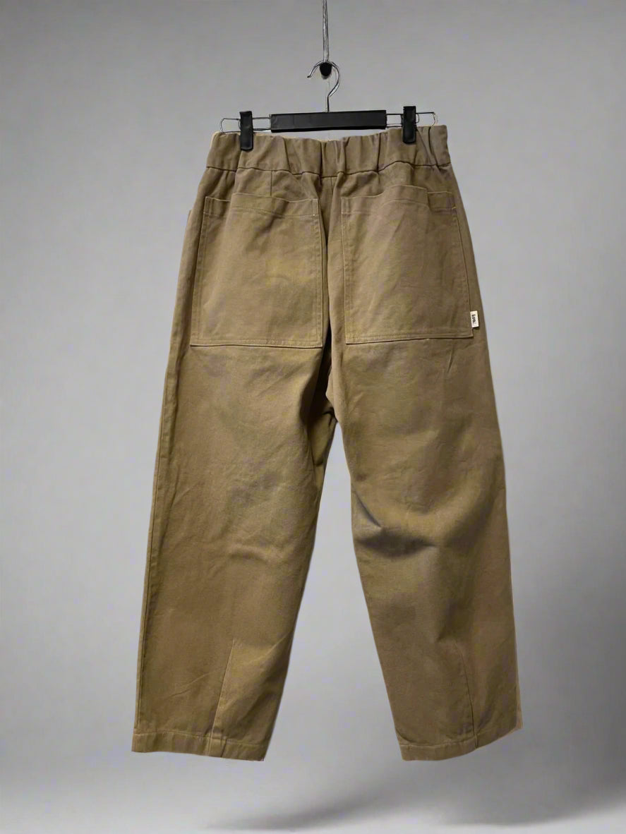 Brown pants hanging on a hanger against a white wall