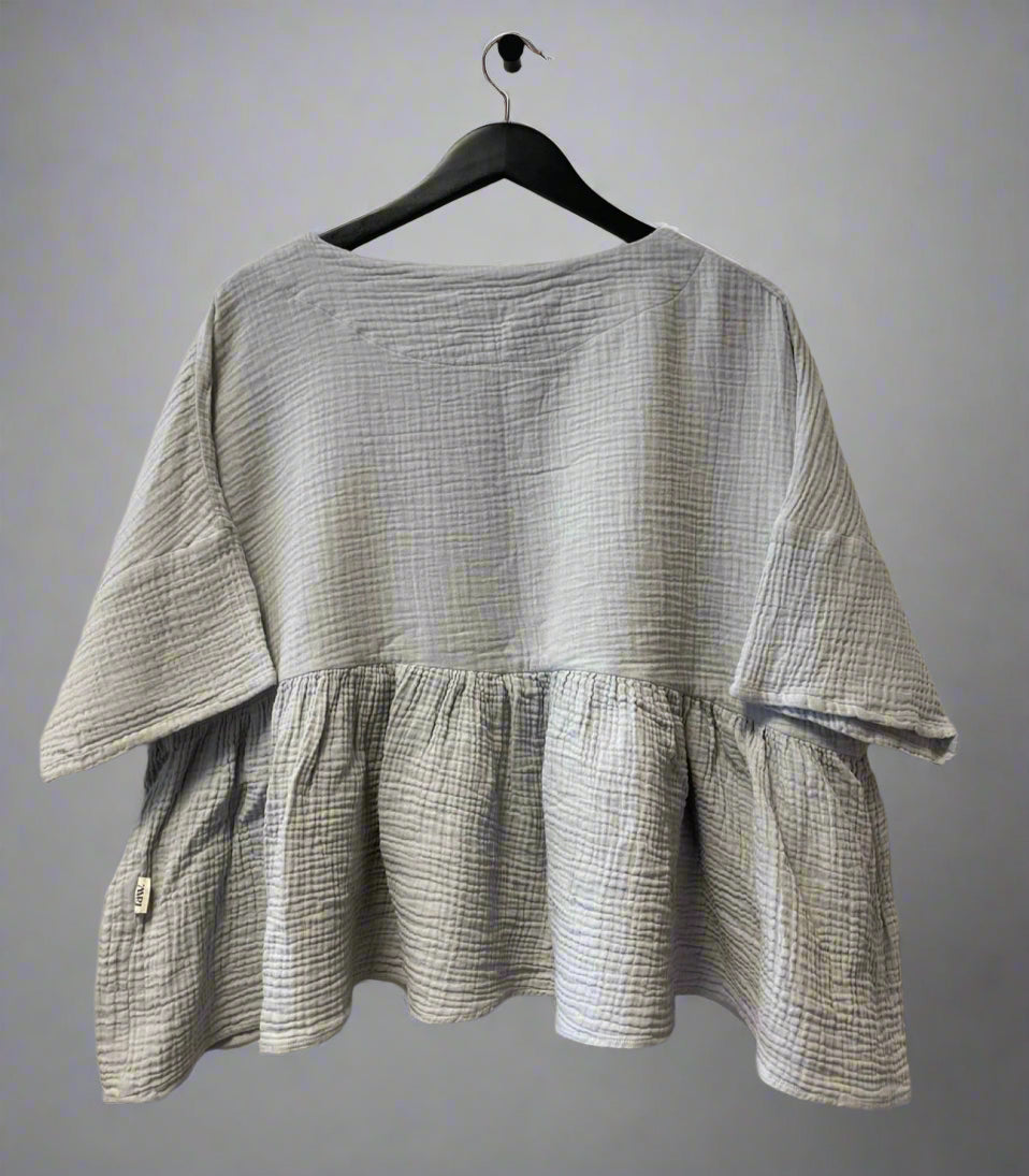 Checkered blouse with ruffled bottom hanging on a hanger against a white wall.