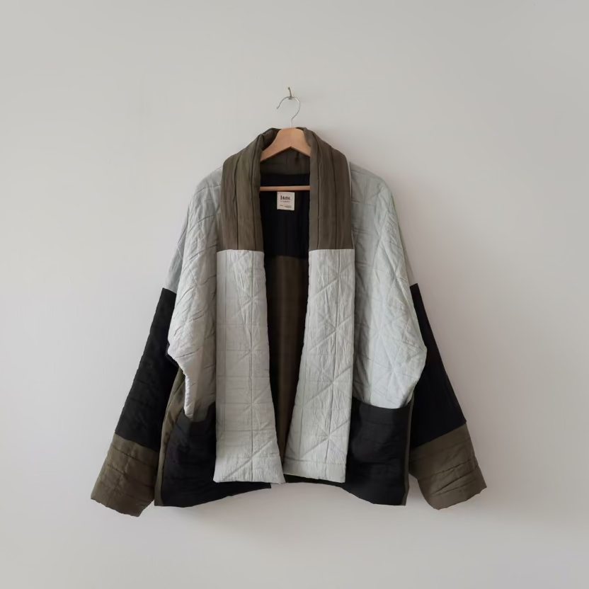 Quilted jacket with color-block design on a hanger against a white wall
