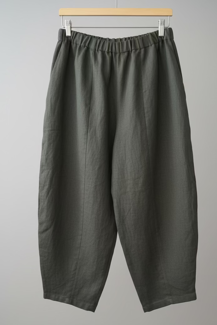 Dark gray pants hanging on a wooden hanger against a white wall.