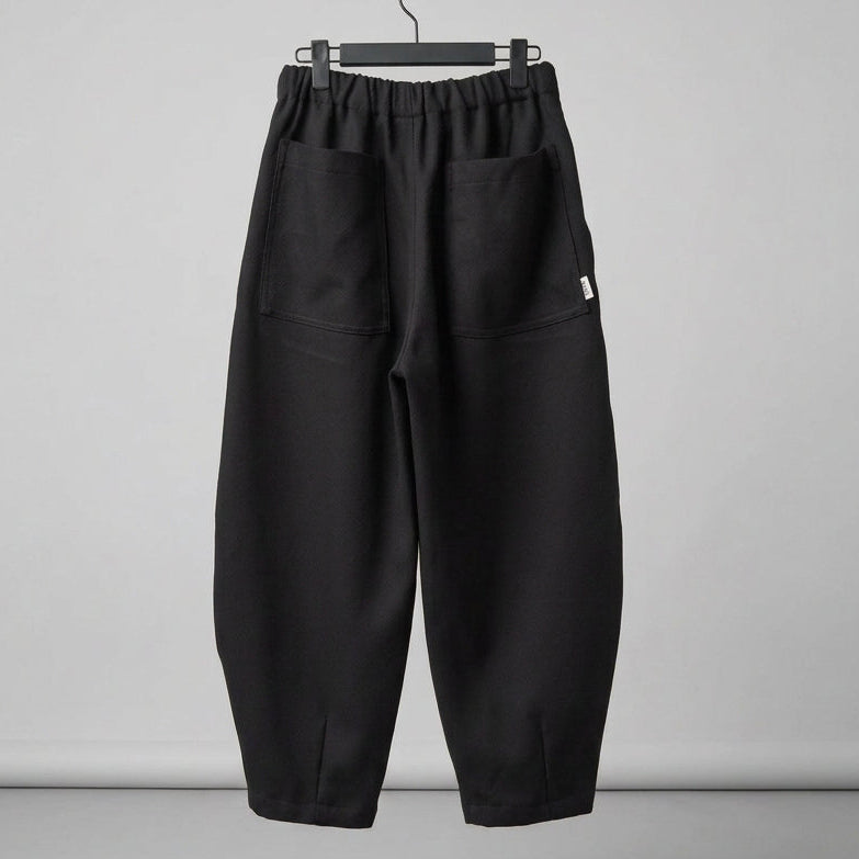 Black wide-leg cropped pants with an elastic waistband and large patch pockets, hanging on a black hanger against a white wall.