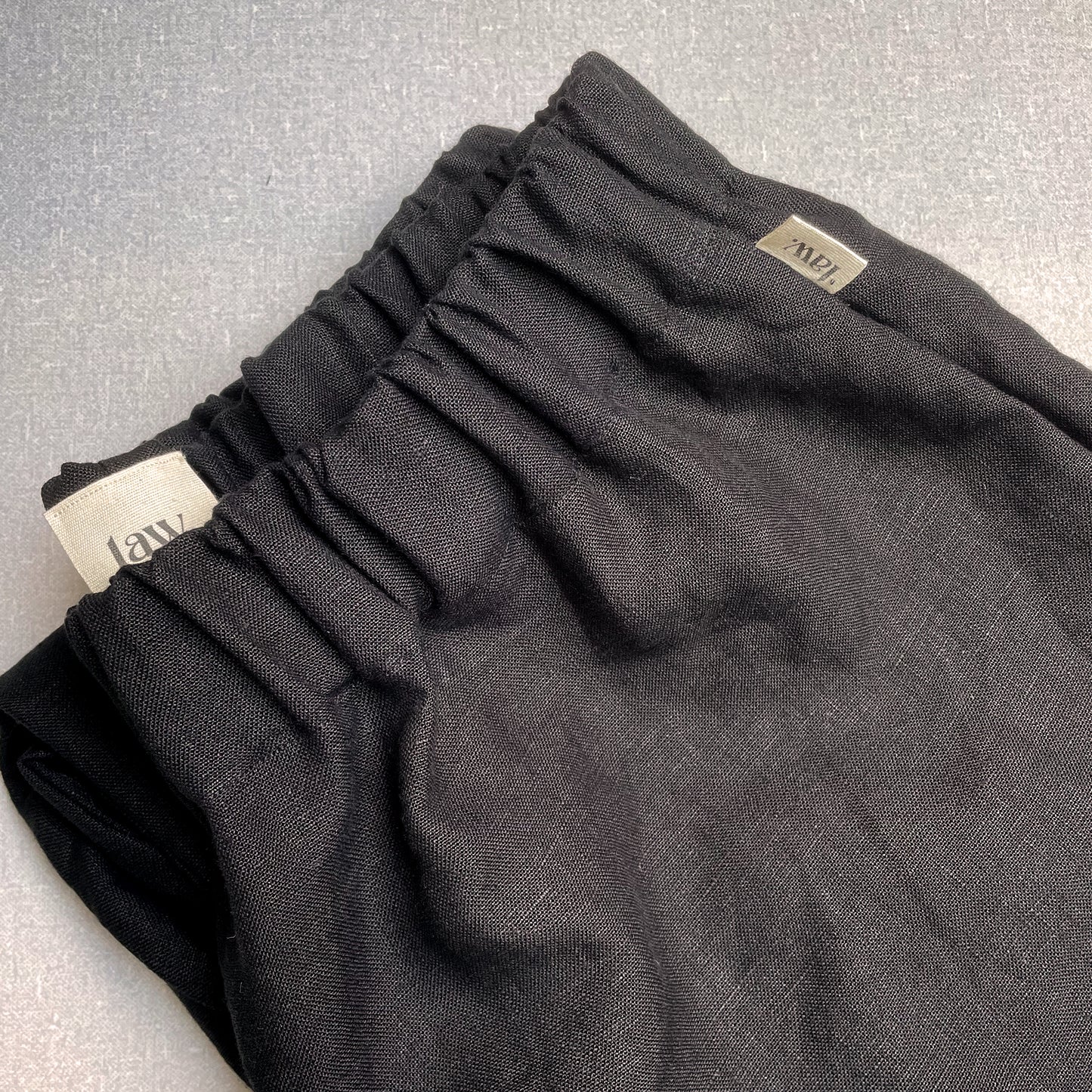CLOSE UP OF BLACK LINEN TROUSERS WITH COTTON TAB